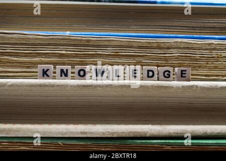 Primo piano di conoscenza di parola isolata scritto da piastrelle di legno di lettera su palo con vecchi libri gialliti Foto Stock