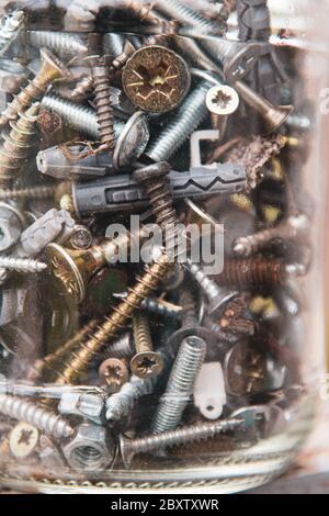 Foto grunge attraverso un vaso di vetro sottile e sfocato con vecchi bulloni e dadi in metallo. Messa a fuoco morbida su raccordi di fissaggio in metallo con bordi sfocati del telaio Foto Stock