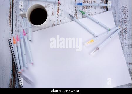 su un tavolo bianco di legno si trova un album con molte penne e pennarelli e una tazza di caffè.c'è un posto per il testo. Foto Stock