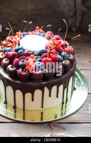 Torta di compleanno con cioccolato fuso, ciliegia fresca, lampone, fragola, ribes rosso, mirtillo su sfondo rustico di legno. Foto Stock