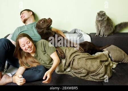Divertente coppia pazza che si ferma a casa con cane labrador riever e carino gatto, ritratto di famiglia sul divano, PET terapia Foto Stock