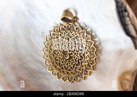 Pendente in ottone con simbolo om in loto forma rotonda mandala su sfondo bianco conchiglia Foto Stock