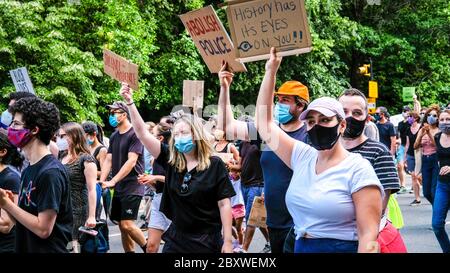 I marchers indossano maschere che tengono i segni di protesta ad una marcia a Brookyn Foto Stock