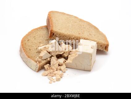 Blocco di lievito fresco sbriciolato su due fette di pane su sfondo bianco. Foto Stock