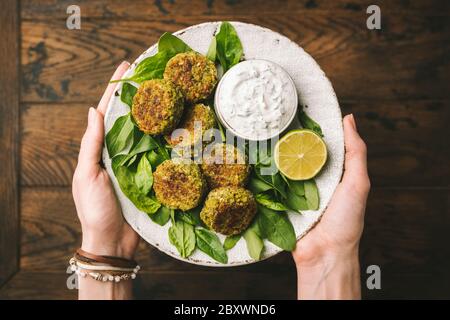 Falafel con salsa allo yogurt tzatziki. Piatto di spinaci vegetariani con le mani della donna, servito con salsa tzatziki di yogurt greco Foto Stock