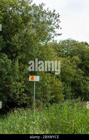 Questi segnali di avvertimento sono su un percorso che conduce attraverso un bosco a stagno di pesca locale. Avvertono di linee elettriche aeree. Foto Stock