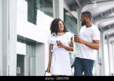 Happy Black Man e Donna a piedi con caffè vicino all'edificio dell'aeroporto Foto Stock