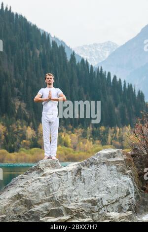 Un giovane in bianco pratica yoga in montagna. Posa Samastiti namaskar Foto Stock