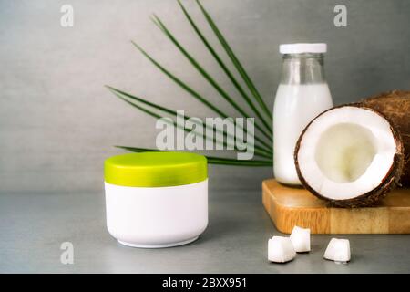 Crema Spa per la pelle del corpo e i capelli con olio di cocco, noci di cocco fresche, foglia di palma e bottiglia con burro di cocco su sfondo grigio scuro. Cosme naturale Foto Stock