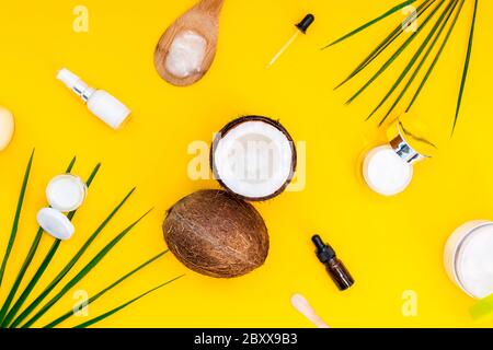 Vista dall'alto cosmetici naturali biologici per la pelle del viso e del corpo con olio di cocco su sfondo giallo. Noci di cocco fresche e diversi contenitori di crema e. Foto Stock