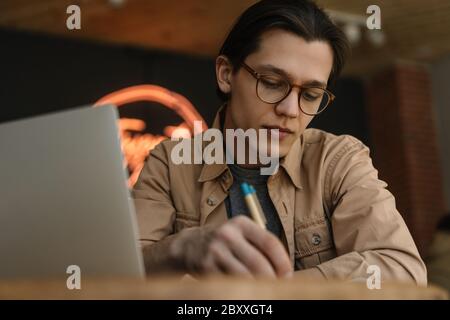 Bell'uomo che lavora progetto freelance, strategia di pianificazione, ricerca di informazioni seduto in caffetteria. Giornalista pensivo che scrive un articolo sul posto di lavoro Foto Stock