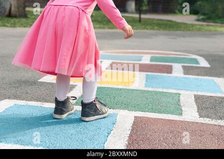 Bambina in un abito rosa che gioca hopscotch sul parco giochi all'aperto, attività all'aperto per bambini Foto Stock