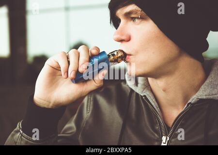 Un giovane uomo in una giacca nera in pelle fuma un vape. Foto Stock