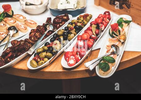 Antipasto Peppers di ciliegia dolce ripieni di formaggio morbido, olive con olio, pomodori secchi e involtini di formaggio. Piatti di ceramica su tavola di legno. Foto Stock