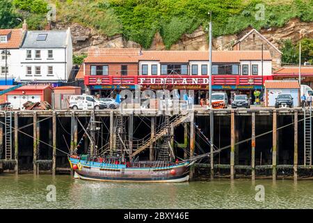 I portici Funland, Family Entertainment e Millers presso il porto di Whitby, dove è ormeggiato il piccolo Bark Endeavour Whitby, Scarborough, Inghilterra Foto Stock