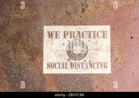 Un segno appostato sul pavimento di un'istituzione di alimentazione che dichiara, 'praticiamo l'allontanamento sociale.' Foto Stock