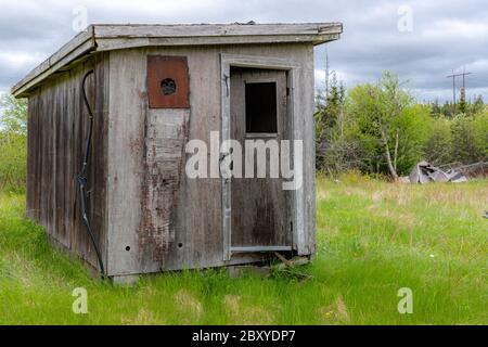 Un piccolo barattino di legno abbandonato in un campo. La porta è leggermente socchiusa. Cielo scuro e coperto. Foto Stock