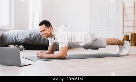 Uomo che si esercita al portatile facendo Plank durante l'allenamento online in interni Foto Stock