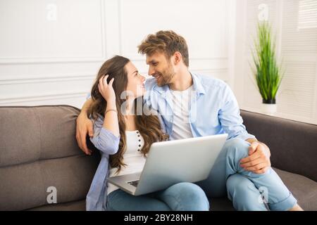 Giovane coppia in denim seduta su un divano che si guarda l'un l'altro e si sente felice Foto Stock