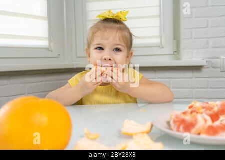4 anni bambina in una blusa gialla mangia pompelmo con piacere Foto Stock