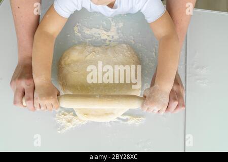 papà e bambino rotolano fuori l'impasto per una torta con un mattonello. svago della famiglia, attività di autoisolamento con un bambino Foto Stock