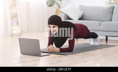 Home Training. Donna musulmana che fa lo yoga in fila davanti al laptop Foto Stock