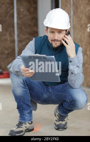 giovane handyman che tiene gli appunti in mano e fa la chiamata Foto Stock