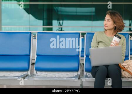 Tempo di caffè. Donna attraente seduta nella sala dell'aeroporto, bevendo caffè e lavorando su un computer portatile Foto Stock