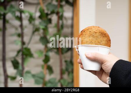 Tenere a mano una tradizionale fritta coreana fritta fritta frittella, Hotteok, con ripieni dolci in una tazza. Popolare cibo di strada coreano. Foto Stock