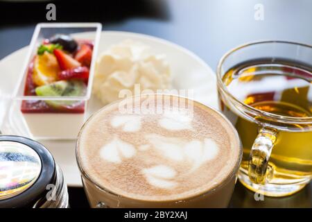 crema di fragole e una tazza di tè e caffè su sfondo di legno, fuoco selettivo Foto Stock