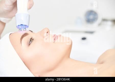 Procedura di estetica della luce microcorrente. Bellezza faccia ragazza. Macchina cosmetologica Foto Stock