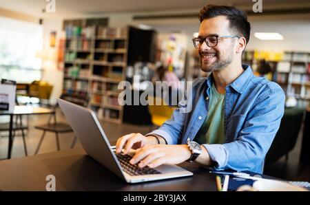 Sorridente studente maschile che lavora e studia in una biblioteca Foto Stock