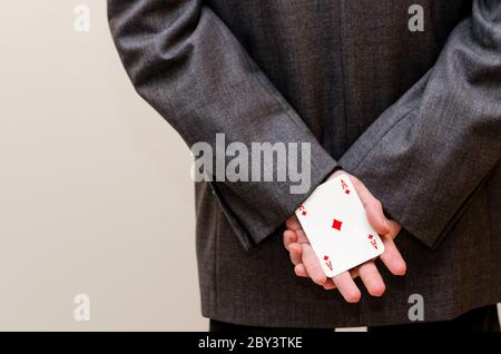 Uomo d'affari che tiene una carta d'asso nelle mani, nascosto dietro di lui Foto Stock