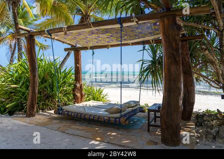 Altalena in legno con materasso e cuscini sotto un baldacchino sulla spiaggia tropicale vicino al mare, isola Zanzibar, Tanzania, Africa orientale, viaggi e vacanza co Foto Stock