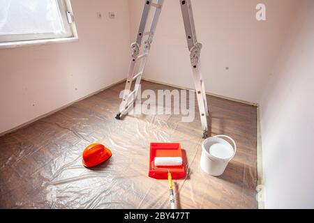 Attrezzi di verniciatura scala a rulli e vernice bianca in preparazione per la verniciatura di piccoli locali vuoti Foto Stock