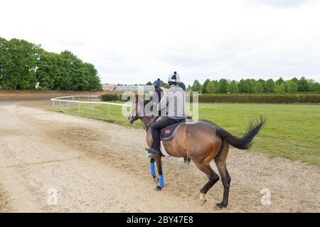 Coppia di piloti visti su cavalli da galoppo in uno spazio pubblico aperto. Vista adiacente a recinzioni e una strada deserta, che conduce dalla cima di una collina. Foto Stock