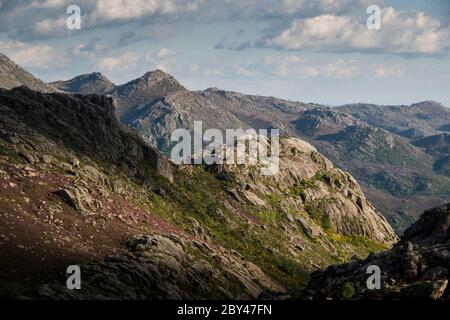 Armoniosa vista della catena montuosa rocciosa ricoperta da una colorata vegetazione primaverile sotto un cielo blu nuvoloso, con ombre nuvolose sulle cime. Orizzontale Foto Stock