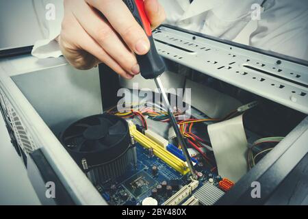 Primo piano sulle mani con l'attrezzo cacciavite del tecnico che ripara un calcolatore del PC Foto Stock