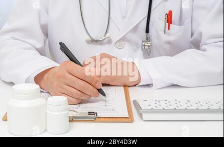 Le mani di un medico maschile che scrive una carta medica. Foto Stock