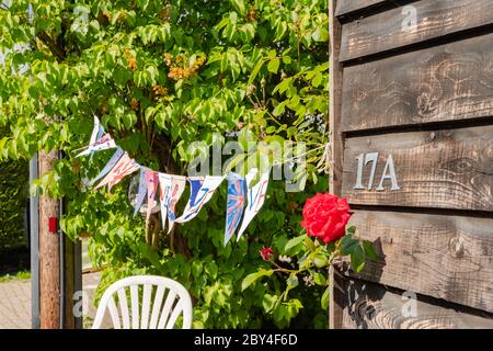 Il mungere di Union Jack fatto a mano si è visto sparso da un garage di legno ad un palo di legno, durante le celebrazioni del giorno di VE Street party. Foto Stock