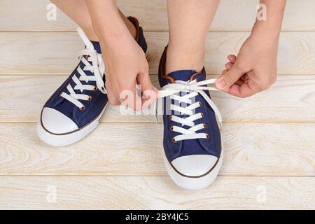 Le mani caucasiche legano lacci elastici bianchi su classiche sneakers blu o scarpe da ginnastica per interni. Scarpe comode per il fitness e lo sport. Scarpe con allacciatura. Foto Stock