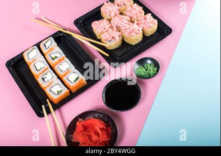 Panini sushi con salsa di maionese rossa e Philadelphia in scatola nera. Consegna di cibo. Sfondo rosa e blu Foto Stock