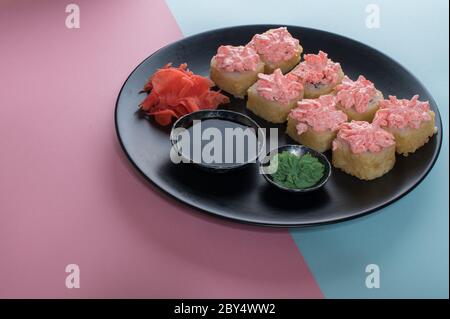 Panini al sushi con salsa alla maionese rossa serviti su piatto nero. Sfondo rosa e blu Foto Stock