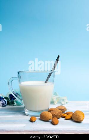 Latte di mandorle in un bicchiere su fondo blu con noci Foto Stock