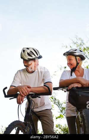 La vecchia donna e l'anziano con casco e bicicletta vanno in bicicletta Foto Stock