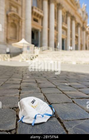 Maschera medica usata su pietre di pavimentazione di un st vuoto. Piazza Peters nella città del Vaticano durante la pandemia di Covid 19 Foto Stock