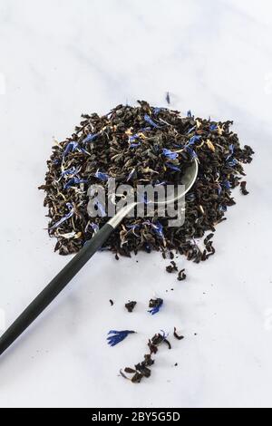 Piccola pila di tè grigio con fiori blu e un piccolo cucchiaino da tè su uno sfondo di marmo bianco Foto Stock