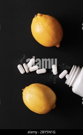 Capsule di vitamina C. Pillole con bottiglia di pillola e frutto bio limone isolato su sfondo scuro. Vista dall'alto Foto Stock