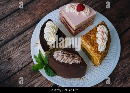 Raccolta di vari dolci su sfondo di legno. Assortimento di pezzi fette con crema. Piatto con diversi tipi di dolci. Diverse fette di deliziosi dessert. Menu pasticceria Foto Stock
