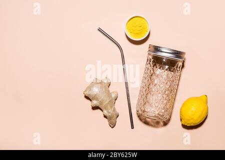 Ingredienti per la preparazione di acqua di zenzero e un elegante vasetto con una paglia metallica su sfondo beige. Foto Stock